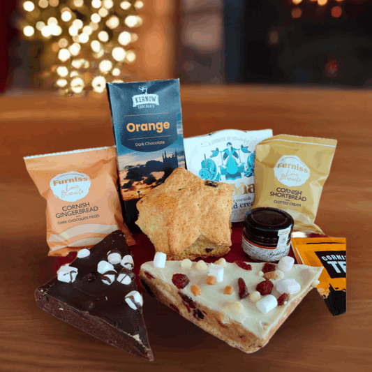 Assorted snacks and treats on a wooden surface with a festive background featuring lights and a fireplace.